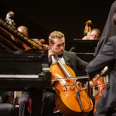 Student playing cello onstage with orchestra